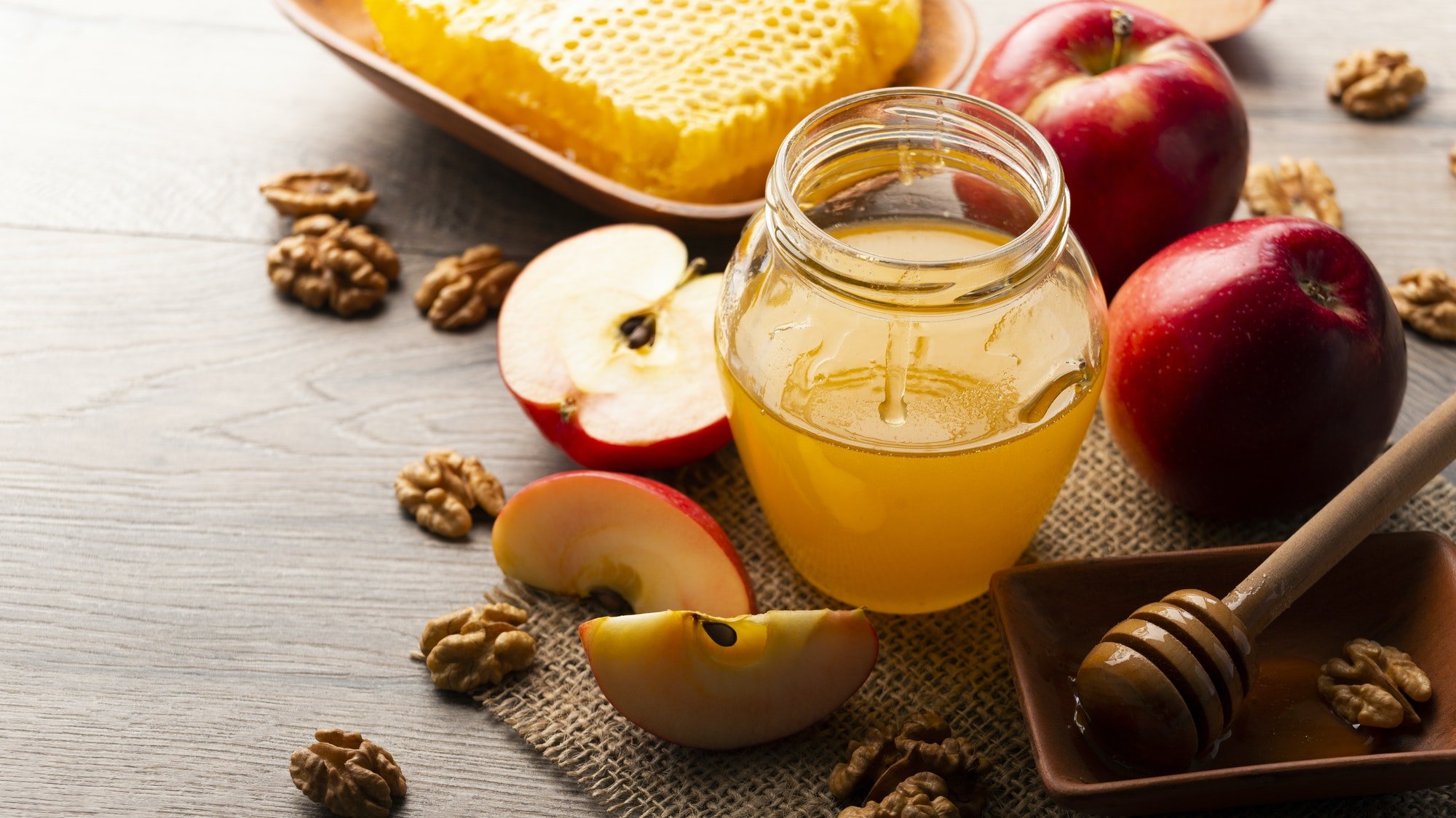 Mason jar with honey, honey dipper, honeycomb, red apples and walnuts on kitchen table